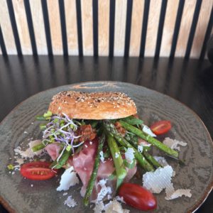 Bagel met roomkaas, rauwe ham, gemarineerde groene asperges, zontomaatjes en Parmezaanse kaas